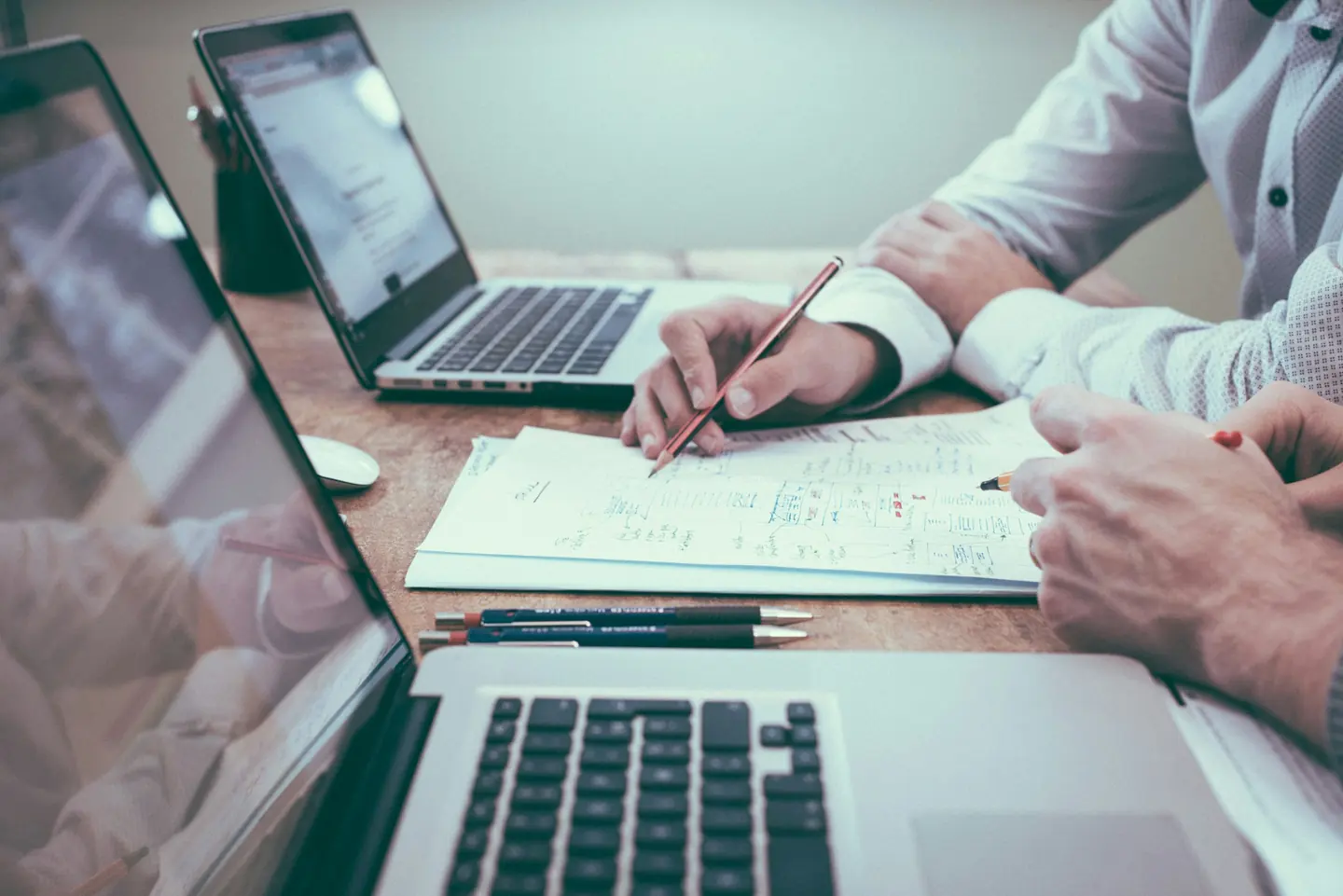 Two people reviewing business plans and notes next to laptops